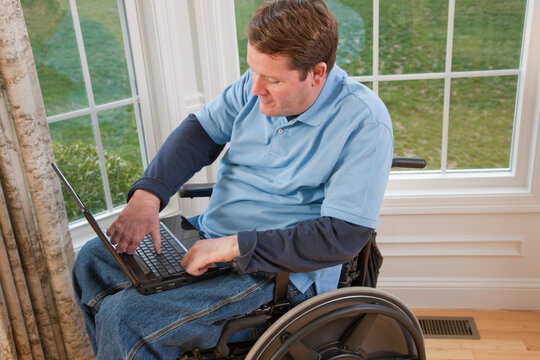 Businessman with spinal cord injury in a wheelchair working on a laptop with disabled hands