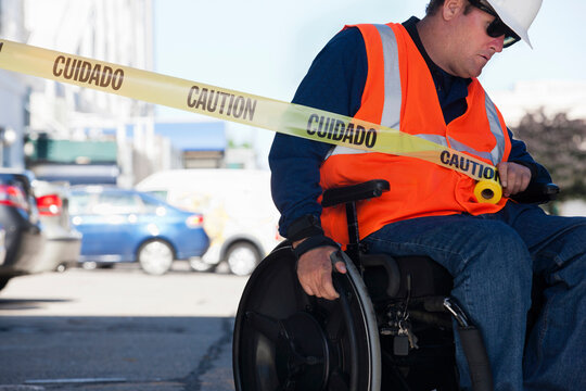 Facilities engineer in a wheelchair pulling caution tape across road