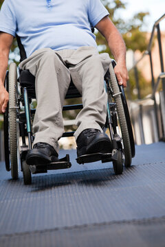 Man with spinal cord injury in wheelchair moving up an outdoor wheelchair ramp