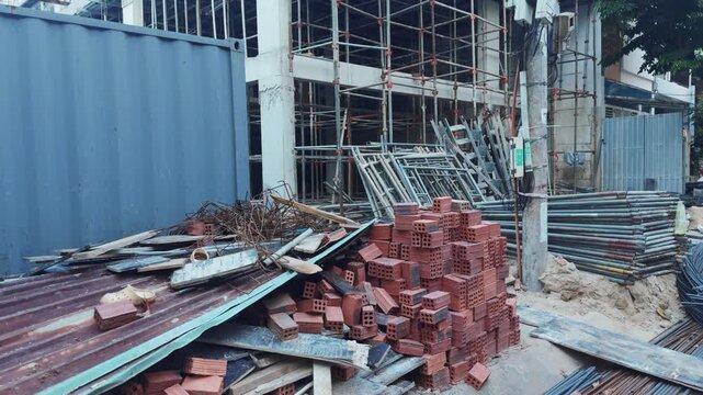 Urban construction site featuring piles of bricks, rusted metal sheets, wooden planks, and rebar near scaffolding and an incomplete building, symbolizing growth and development