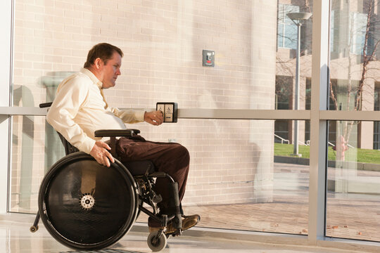 Businessman with spinal cord injury in wheelchair using automatic door opener at office building