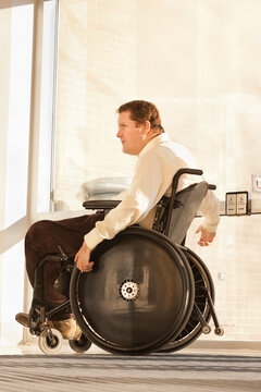Businessman with spinal cord injury in wheelchair using automatic door opener at office building