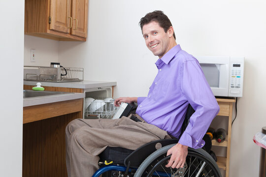 Man in wheelchair with spinal cord injury putting dishes in an accessible dishwasher