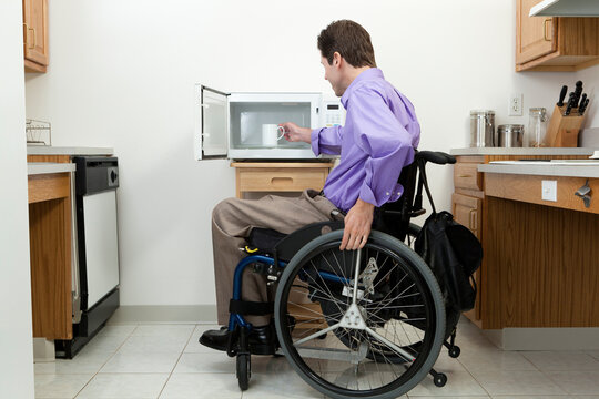 Man in wheelchair with spinal cord injury removing cup from an accessible microwave