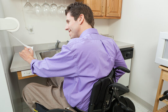 Man in wheelchair with spinal cord injury using a paper towel rack in an accessible kitchen