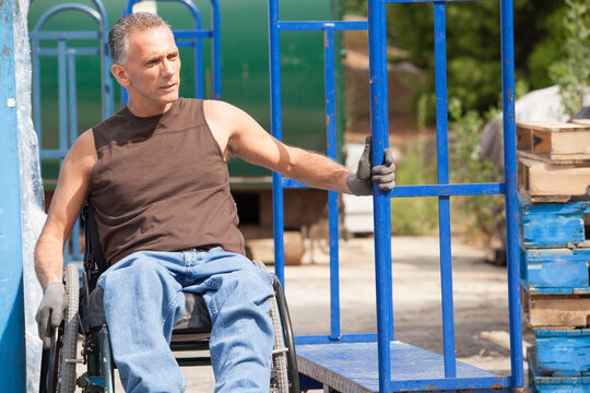 Loading dock worker with spinal cord injury in a wheelchair moving a hand truck