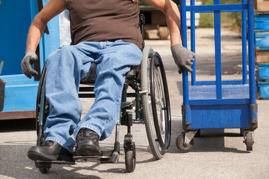 Loading dock worker with spinal cord injury in a wheelchair moving a hand truck