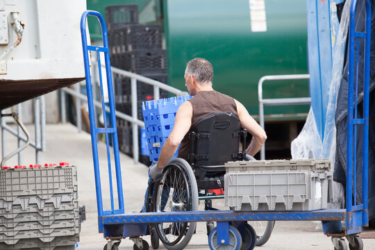 Loading dock worker with spinal cord injury in a wheelchair moving stacked inventory trays