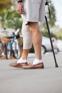 Senior man with bandage on his leg walking with the help of a cane
