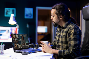 Fototapeta premium Millennial student working from home, engaged in video teleconference with university colleagues, he is utilizing his laptop for the virtual meeting, sitting at a desk, and sharing ideas with others.