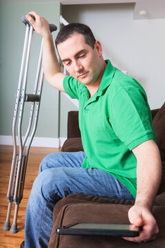 Man after anterior cruciate ligament (ACL) surgery with crutches and an digital tablet at home