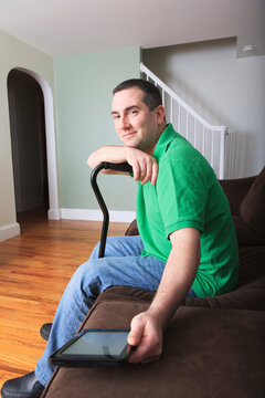 Man after anterior cruciate ligament (ACL) surgery with cane and an digital tablet at home
