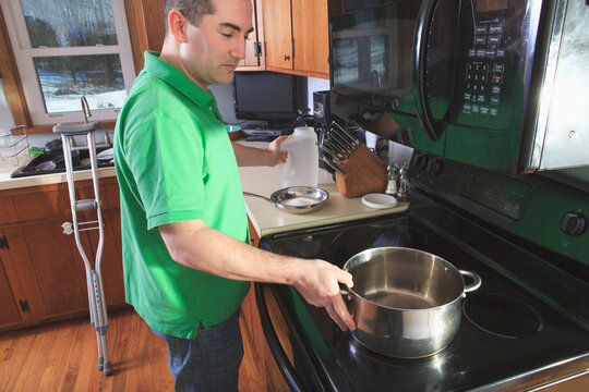 Man after anterior cruciate ligament (ACL) surgery with crutches cooking in the kitchen