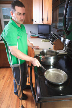 Man after anterior cruciate ligament (ACL) surgery with crutches cooking in the kitchen