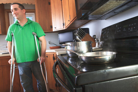 Man after anterior cruciate ligament (ACL) surgery with crutches cooking in the kitchen