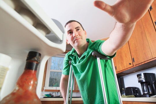 Man after anterior cruciate ligament (ACL) surgery with crutches reaching in his refrigerator in