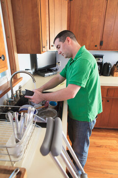 Man after anterior cruciate ligament (ACL) surgery with crutches washing dishes in the kitchen