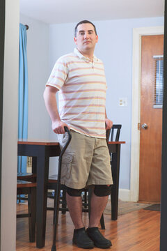 Man after anterior cruciate ligament (ACL) surgery with his cane and knee braces at home