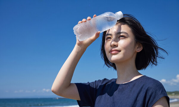 夏の海辺で冷たいペットボトルの水を額に当て涼む女性 夏のＵＶケア 紫外線対策