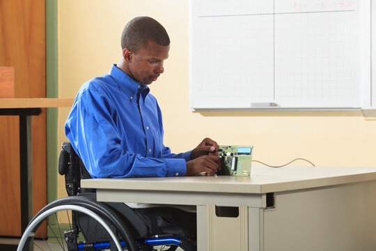 Engineering student sitting in a wheelchair examining microprocessor circuit board for electronics