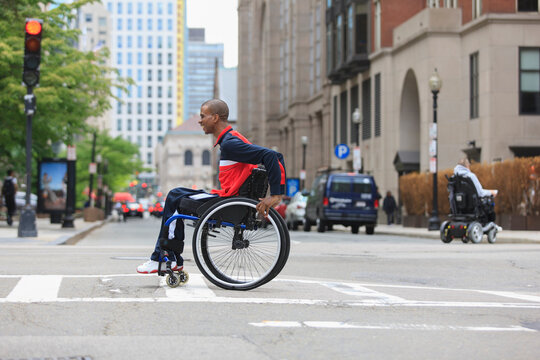 Man in wheelchair who had Spinal Meningitis crossing a city street