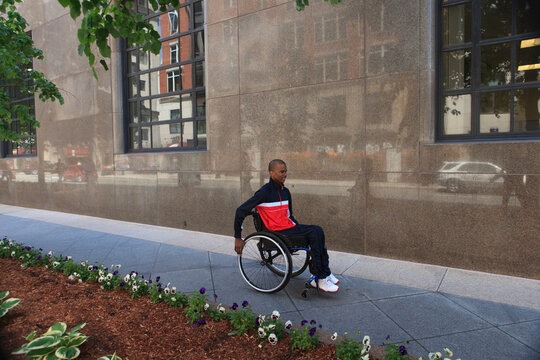 Man in wheelchair who had Spinal Meningitis using a city sidewalk