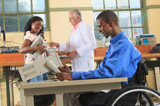 Professor and engineering students in an electronics classroom, one in a wheelchair preparing