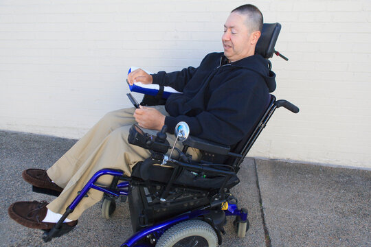 Man with spinal cord injury and arm with nerve damage in motorized wheelchair looking at smart phone