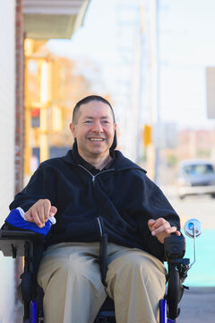 Man with spinal cord injury and arm with nerve damage in motorized wheelchair crossing public street