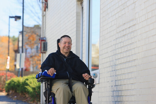 Man with spinal cord injury and arm with nerve damage in motorized wheelchair using a public street