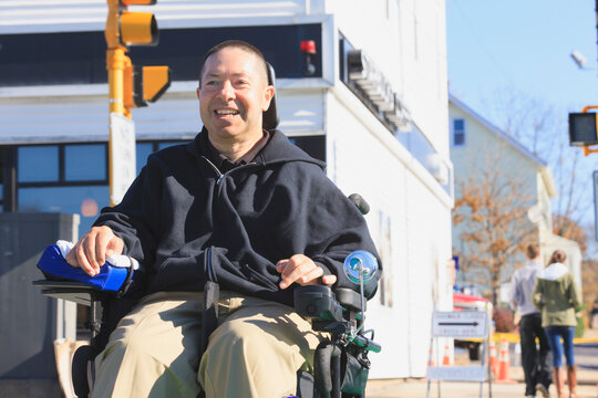 Man with spinal cord injury and arm with nerve damage in motorized wheelchair crossing public