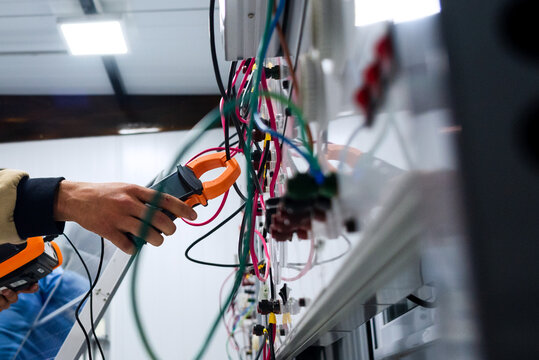 echnician using a clamp meter to measure electrical current in a solar training system.