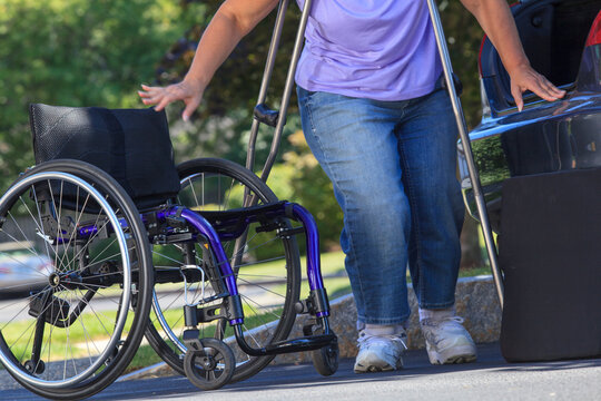 Woman with Spina Bifida about to sit in wheelchair after putting it together outside car