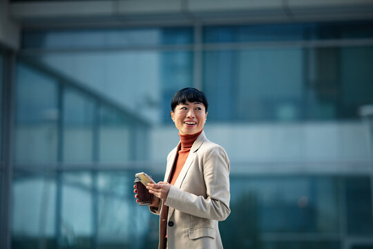 Smiling businesswoman with smartphone and coffee outside office