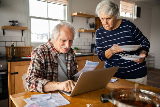 Senior couple reviewing bills on laptop in kitchen