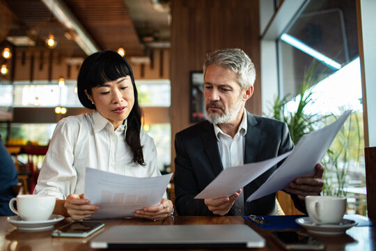Two business colleagues reviewing financial documents at a cafe
