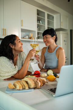 Two women toasting wine while cooking in a home kitchen