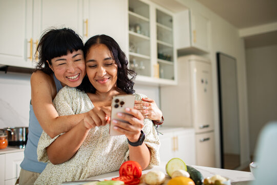 Two women using smartphone while cooking in home kitchen