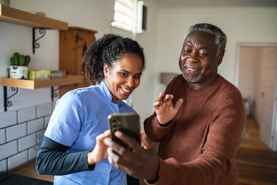 Caregiver helping senior with smartphone video call in home kitchen