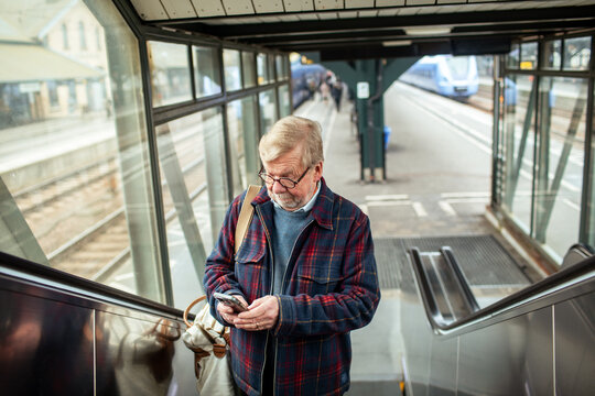 Senior man using smartphone on escalator at train station