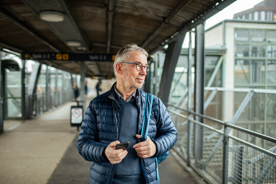 Senior man waiting with smartphone at train station platform