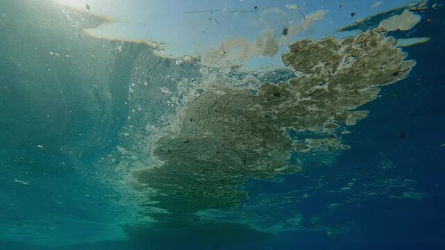 Thick layer of fatty film mixed with plastic trash drifts on the surface of the blue ocean, blocking out the sunlight underwater on a bright sunny day during the doldrums