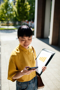 Smiling professional checking smartphone with report in city