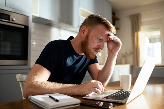 Worried man working on laptop at home kitchen table