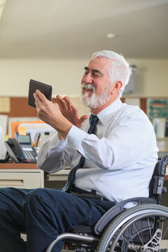 Man with Muscular Dystrophy in a wheelchair using a tablet at his office desk