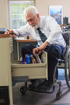 Man with Muscular Dystrophy in a wheelchair taking files of information from his desk drawer