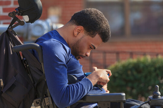 African American man with Cerebral Palsy using a cell phone on his power wheelchair outside