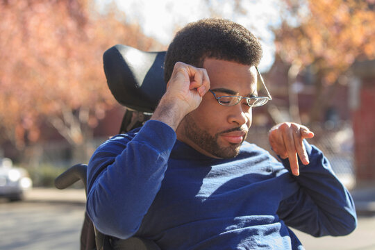 African American man with Cerebral Palsy putting on eyeglasses on his power wheelchair outside