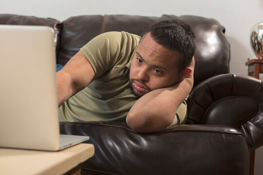 African American man with Down Syndrome using a laptop from his sofa at home