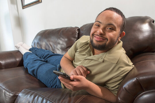 Happy African American man with Down Syndrome using a cell phone on sofa at home